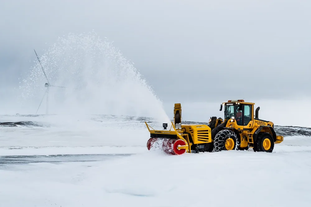 Gul Volvo hjullaster fra Kyllo Maskin med Øveråsen snøfreser kaster snø til siden i åpent vinterlandskap