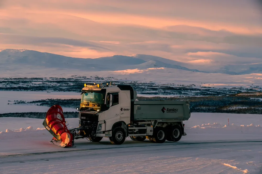 Ramlos-Volvo med tippkasse og rød snøplog på snøklett vidde i gylden kveldshimmel