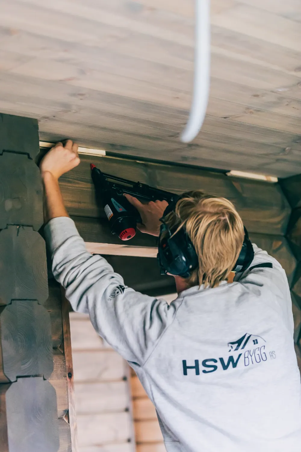 HSW Bygg-arbeider med vernehørsel monterer listverk med spikerpistol i laftebygg