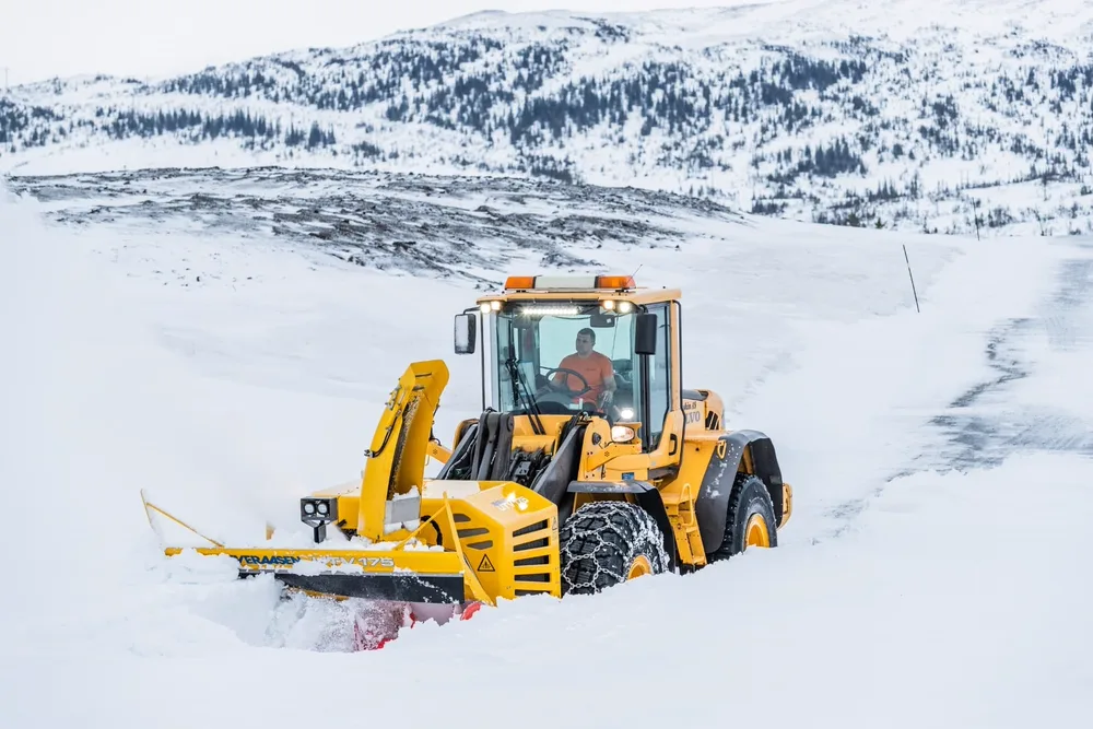 Sjåfør i gul Volvo hjullaster med Øveråsen snøfreser rydder dyp snø på fjellvei