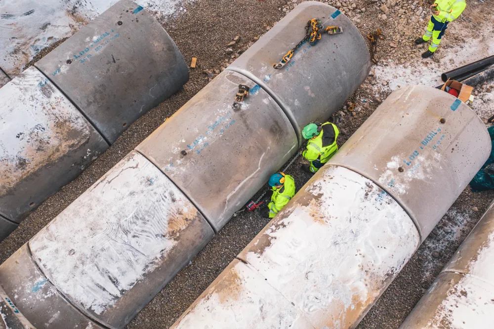 Dronefoto av anleggsarbeidere mellom store rørseksjoner på vinteranlegg